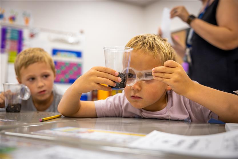 A boy holds up a clear cup with a seed in it